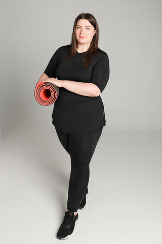Well Fit Activewear. Female model wears black, lightweight, short sleeve, tunic-style gym top with black gym leggings. Well Fit tops and leggings are available in UK sizes 8 to 30. Free shipping over £100.