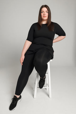 Well Fit Activewear. Female model wears short sleeve black compression gym top in a longer length tunic style and black compression leggings to the ankle. Well Fit tops and leggings are available in UK sizes 8 to 30. Free shipping over £100.