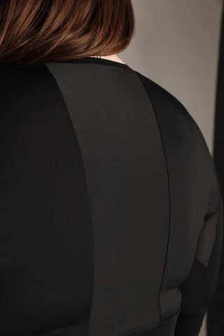 Well Fit Activewear. Female model wears black, lightweight, long sleeve, tunic-style gym top with black gym leggings. Well Fit tops and leggings are available in UK sizes 8 to 30. Free shipping over £100. Image shows the back of Well Fit training top for plus size women. The back of the top has a sweat-wicking, perforated panel that allows for breathability. 