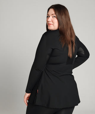 Well Fit Activewear. Female model wears long sleeve black compression gym top in a longer length tunic style and black compression leggings to the ankle. Well Fit tops and leggings are available in UK sizes 8 to 30. Free shipping over £100. Image shows the back of Well Fit training top for plus size women. The back of the top has a sweat-wicking, perforated panel that allows for breathability. 