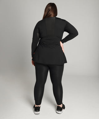 Well Fit Activewear. Female model wears long sleeve black compression gym top in a longer length tunic style and black compression leggings to the ankle. Well Fit tops and leggings are available in UK sizes 8 to 30. Free shipping over £100. Image shows the back of Well Fit training top for plus size women. The back of the top has a sweat-wicking, perforated panel that allows for breathability. 
