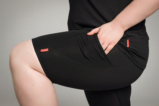 Well Fit Activewear. Female model wears black compression shorts that fall above the knee. The shorts have a pocket on each leg that is big enough for phone, keys, debit card, even a banana as well! Well Fit tops and shorts are available in UK sizes 8 to 30. Free shipping over £100. Model has hand in pocket of the Well Fit compression shorts to demonstrate size and placement.