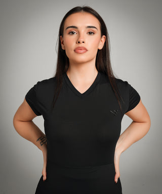 Well Fit Activewear. Female model wears black, lightweight, tunic-style gym top with black gym leggings. Well Fit tops and leggings are available in UK sizes 8 to 30. Free shipping over £100. Model, Jasmine, stands face on to the camera with both hands on hips.